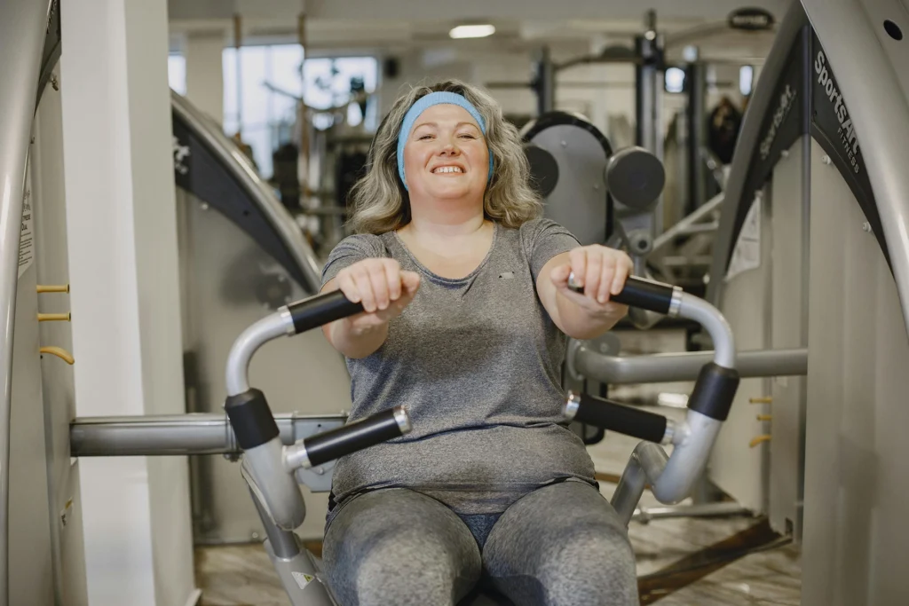 Middle aged women doing the chest press workout in the gym while smiling.